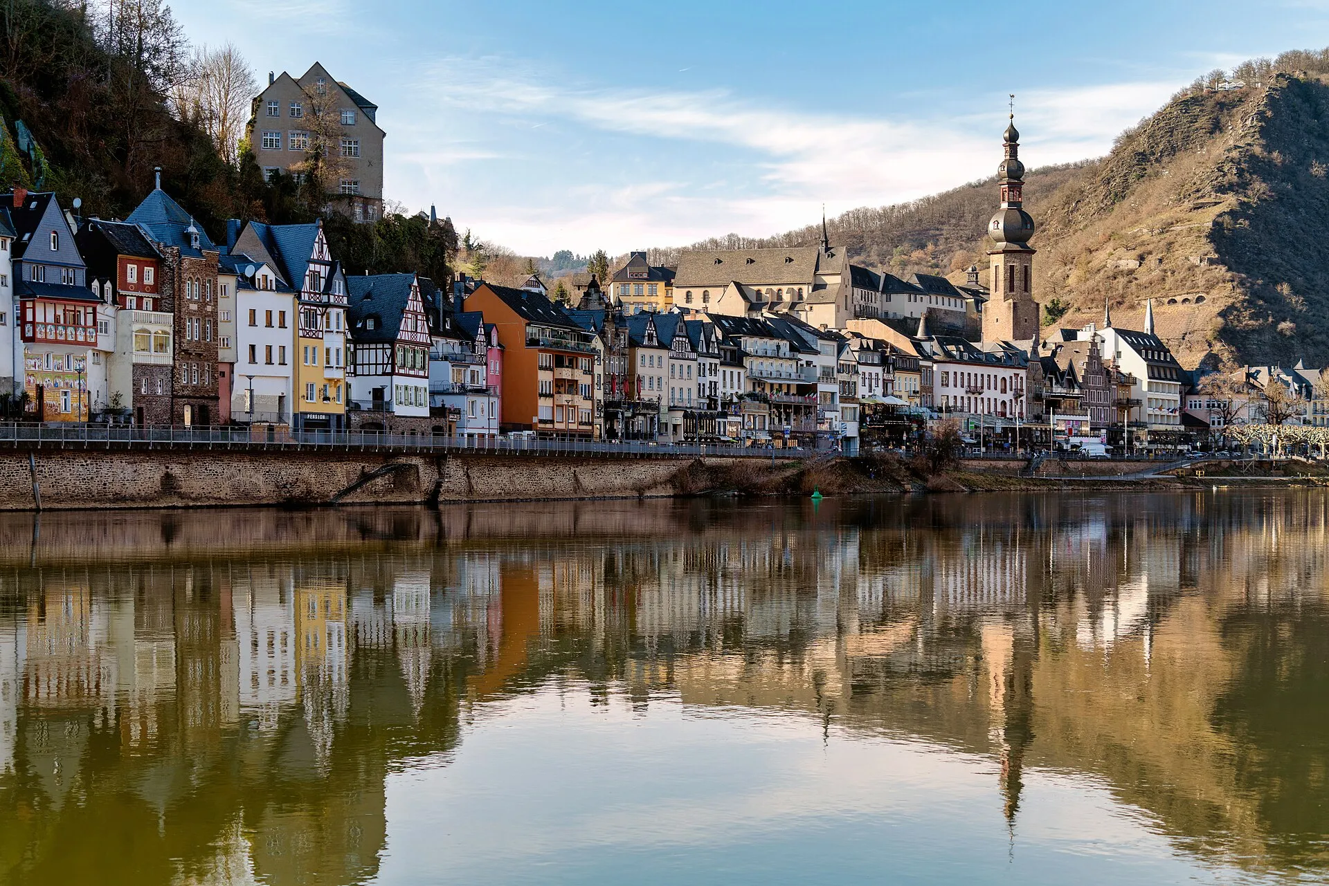 Blick über die Mosel auf die Häuserzeile der Cochemer Moselpromenade mit dem Zwiebelturm von Sankt Martin
