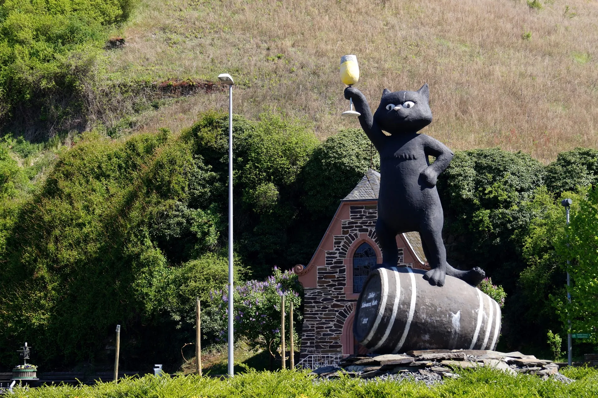 Skulptur der Schwarzen Katz mit erhobenem Weinglas auf einem Weinfass am Ortseingang von Zell