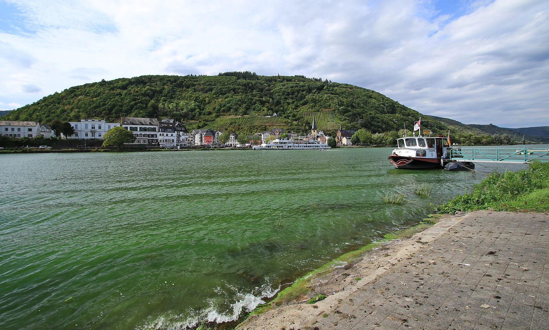 Kleine Personenfähre an einer Anlegestelle der Mosel, gegenüber ein Weinort unter einem bewaldeten Hang