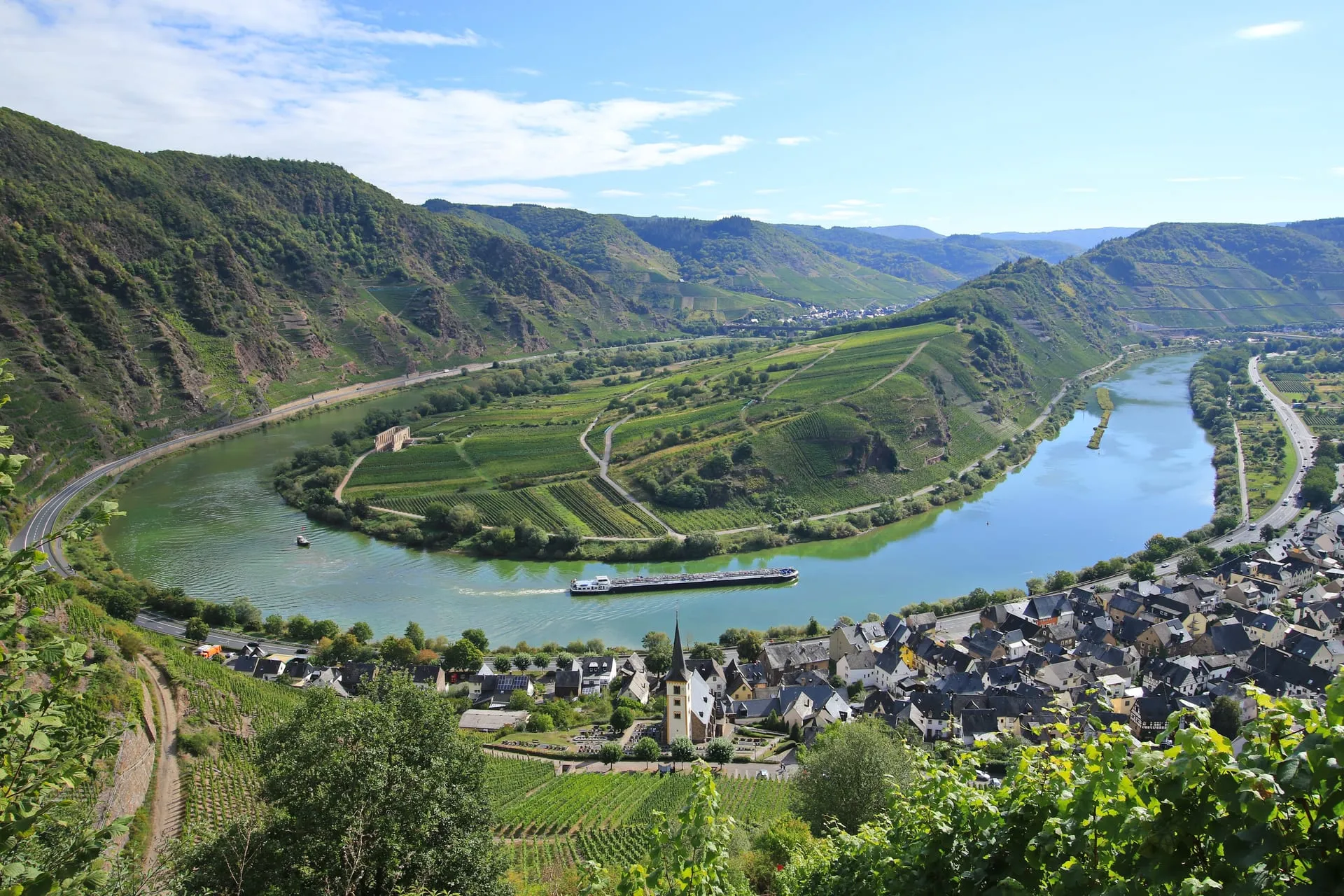 Moselschleife bei Bremm mit Weinbergen, Ortskern und einem Frachtschiff auf der Mosel