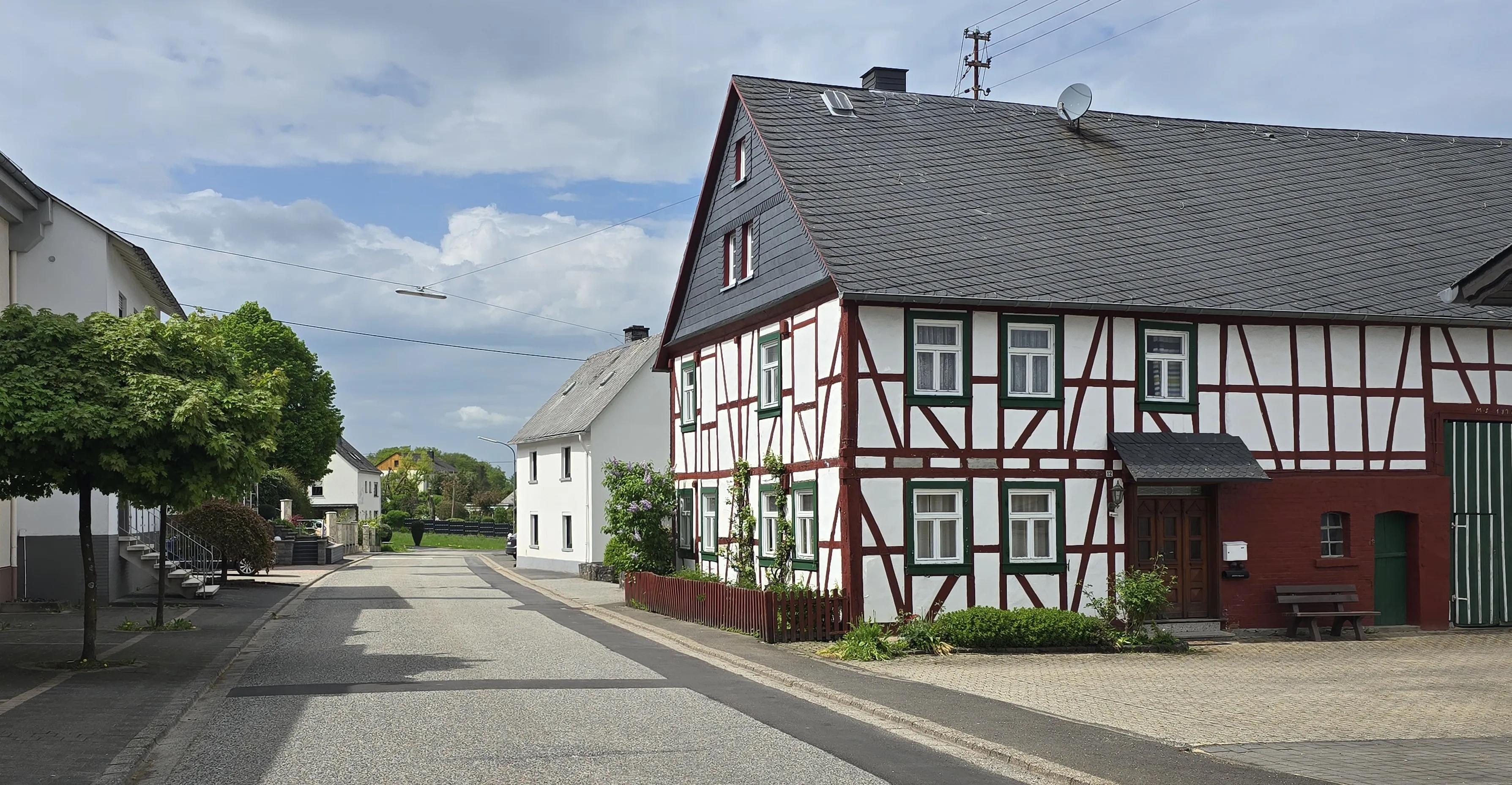 Straßenzug in Blankenrath mit einem rot-weißen Fachwerkhaus, davor ein leerer Fahrbahnabschnitt und ein Baum