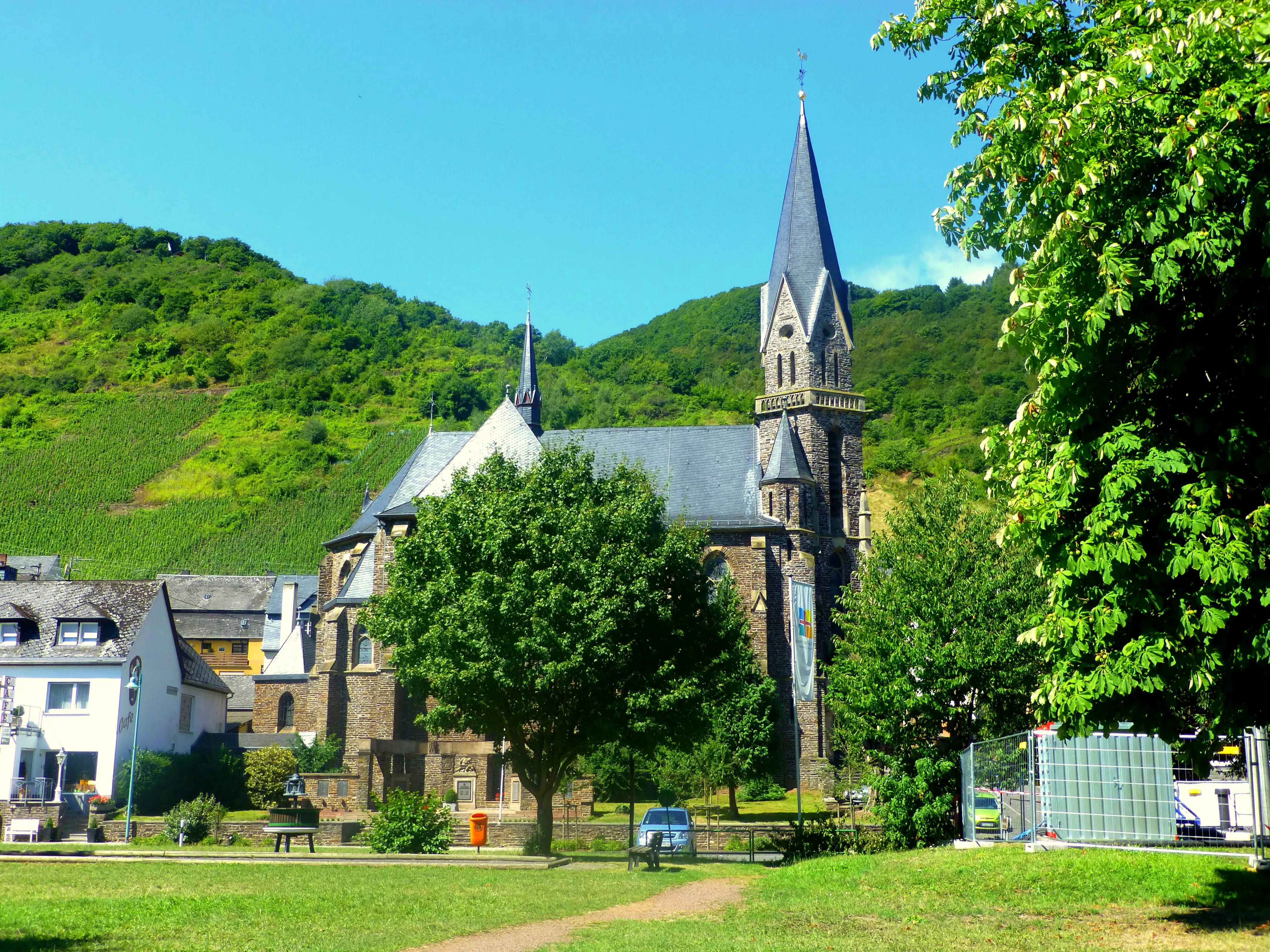 Die neugotische Pfarrkirche St. Bartholomäus in Sankt Aldegund vor bewaldeten Hängen und Weinbergen